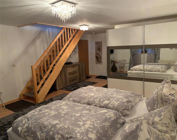 A bedroom with a bed, a wooden staircase, a dresser, a mirror, and a chandelier. - FEWO am Hauchen, 85 qm mit Tiefgarage und Terrasse (Reit im Winkl)