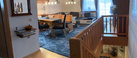 A spacious living area with a dining table, sofa, and a staircase leading to an upper level.