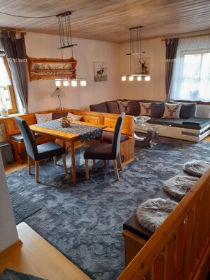 A cozy living room with a wooden dining table, sofa, and a staircase. - FEWO am Hauchen, 85 qm mit Tiefgarage und Terrasse (Reit im Winkl)
