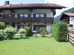 A two-story building with a balcony on the upper floor, surrounded by a well-maintained lawn and bushes. - FEWO am Hauchen, 85 qm mit Tiefgarage und Terrasse (Reit im Winkl)