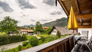 Un balcon avec un parasol jaune, donnant sur un village avec des maisons et des montagnes.