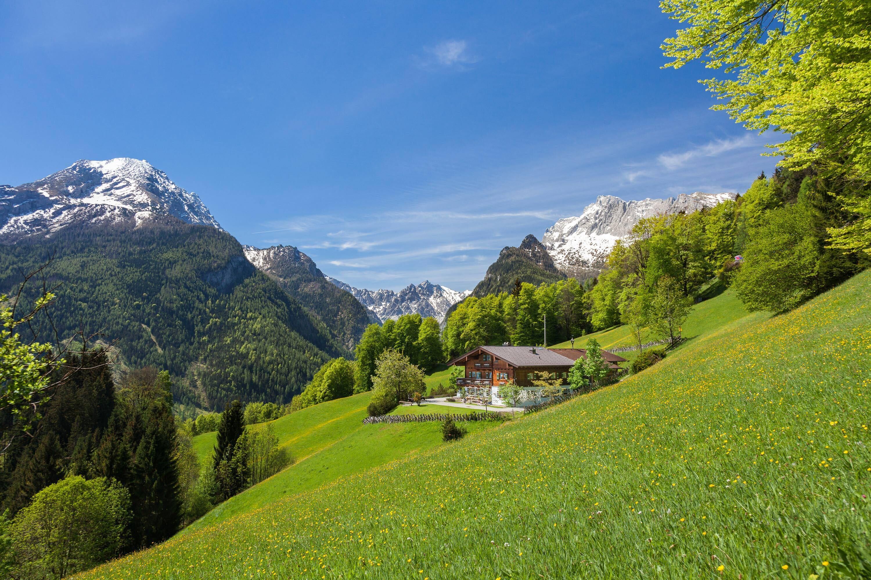 A chalet in a mountainous area with a clear view of snow-capped peaks in the background.