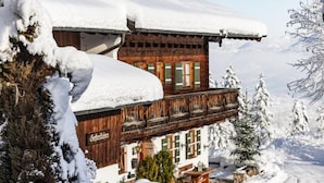 Un chalet en bois doté d’un balcon, entouré d’arbres couverts de neige et avec une chaîne de montagnes en toile de fond.