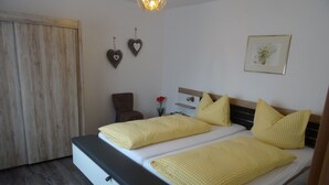 A double bed with yellow checkered bedding, a wooden headboard, and a bedside table with a vase of flowers. - Vacation apartment Josefa, 2 persons, 1 bedroom, kitchenette, terrace, 55 sqm (Inzell)