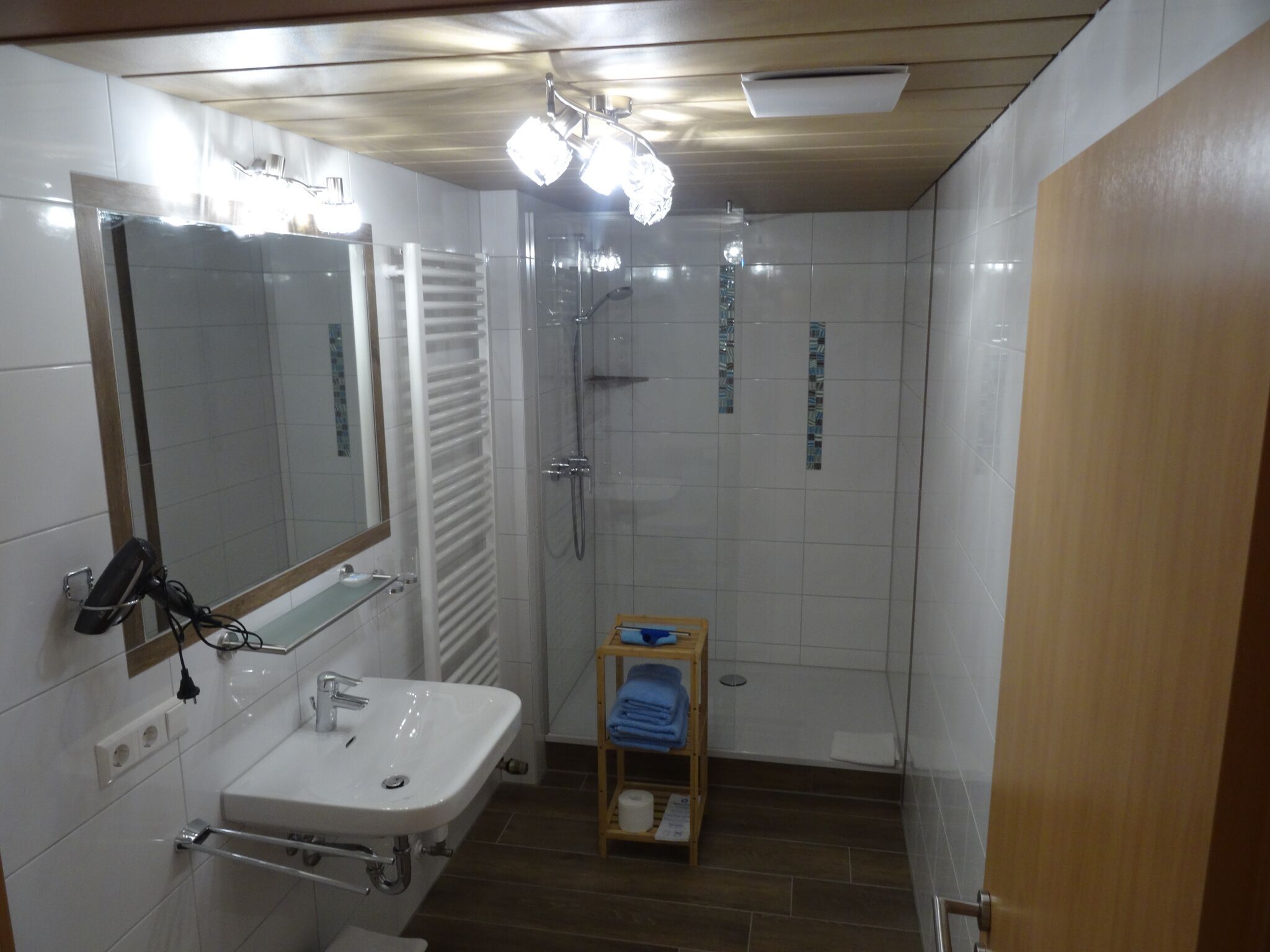 Een badkamer met een wastafel, spiegel, handdoekrek, douche en een klein plankje met handdoeken.