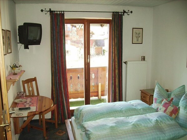 A bedroom with a bed, a chair, a desk, a television, and a window with curtains.