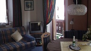 A living room with a sofa, a television, a table with a bottle, and curtains. - Zwei-Raum-Appartement (5) 45qm, Extra-Schlafzimmer mit Dusche/WC, Miniküche, Balkon (Reit im Winkl)