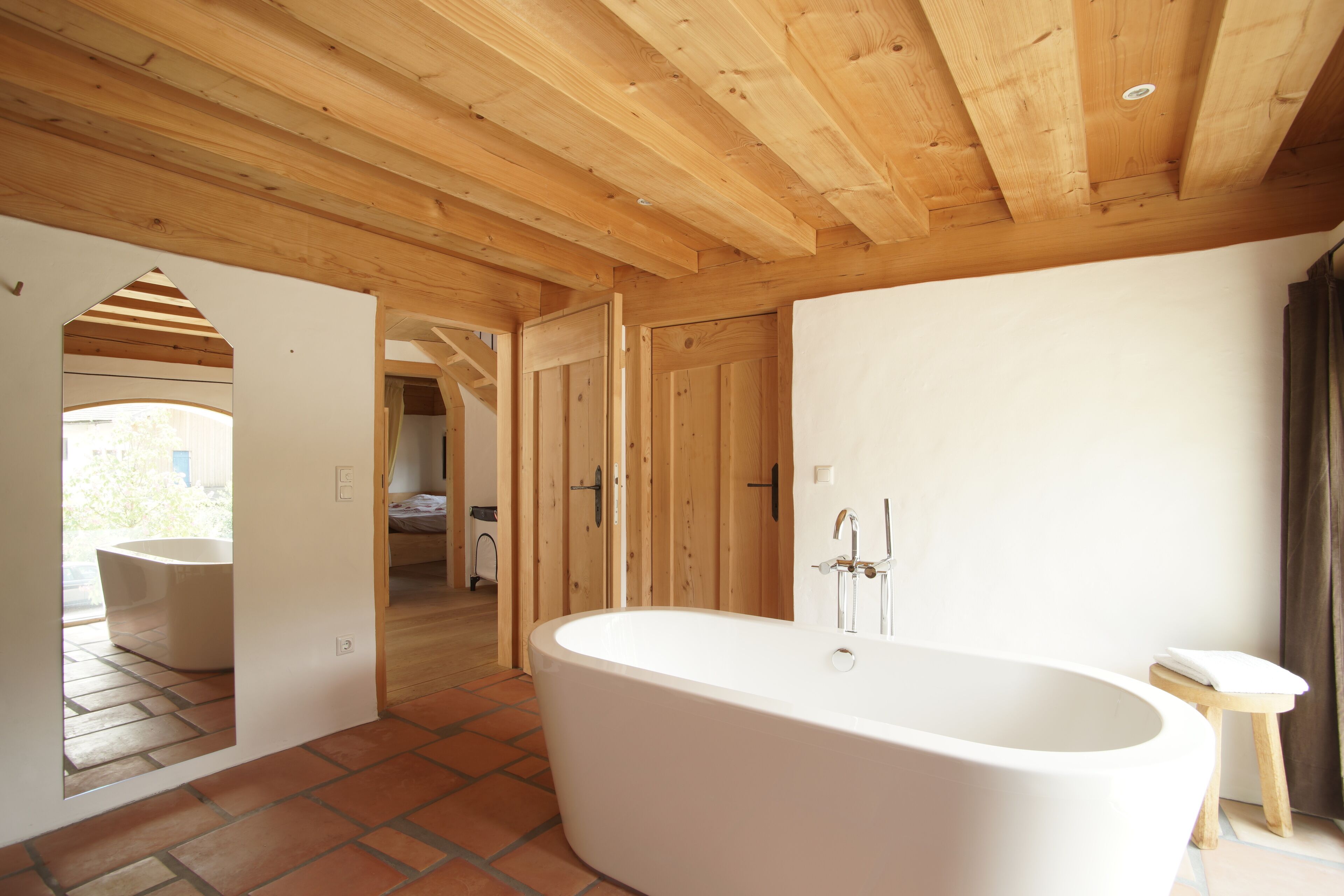 Un baño moderno con una bañera independiente, vigas de madera en el techo y suelo de baldosas.