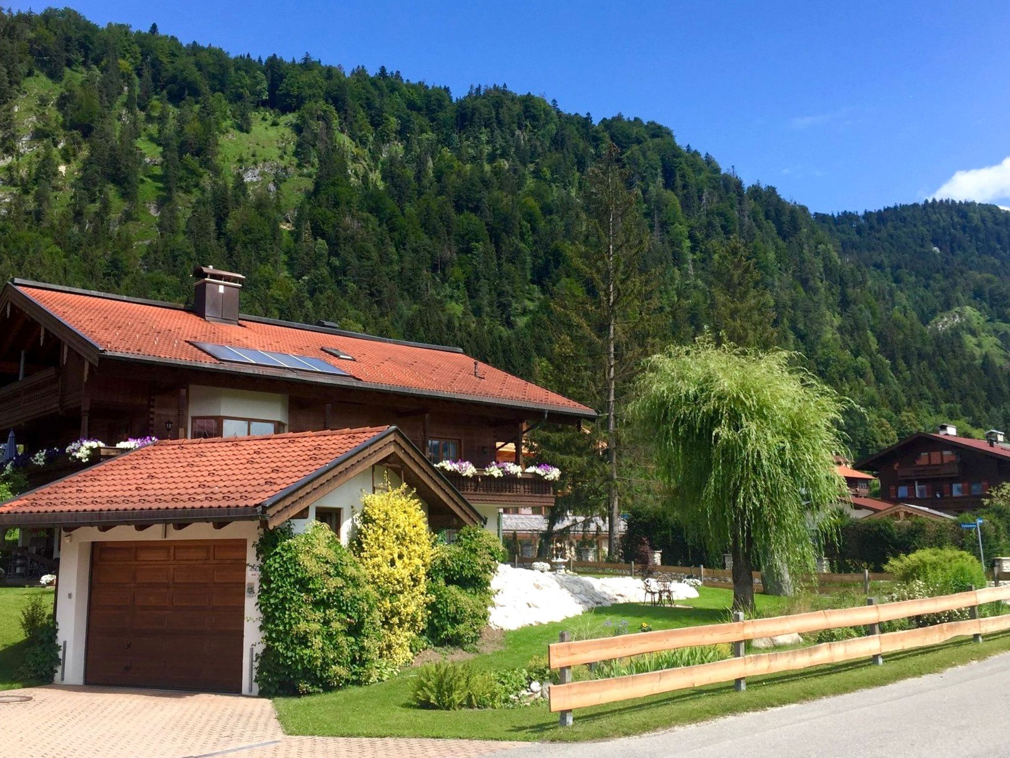 A chalet-style building with a red-tiled roof, a wooden deck, and a garden with various plants and flowers.