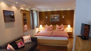 Een slaapkamer met een bed, een bank, een televisie en een houten kast.