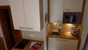 Een compacte keuken met een spoelbak, een koffiezetapparaat en een magnetron. Er zijn kastjes met handgrepen en een klein aanrecht met een boek.