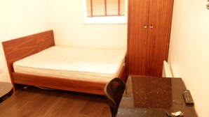 A small, single-bed room with a wooden headboard, a wooden wardrobe, a small table, and a remote control on the table. - SS Property Hub - City of London Studio Apartment 18 (London)