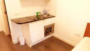 A small kitchenette with a microwave, sink, and a trash bin. - SS Property Hub - City of London Studio Apartment 18 (London)