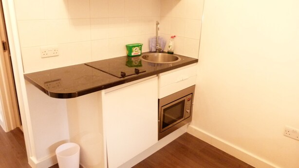 A small kitchen with a black countertop, white cabinets, a stainless steel sink, and a built-in oven. - SS Property Hub - City of London Studio Apartment 18 (London)