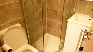 A bathroom with a toilet, a glass-enclosed shower, and a sink. - SS Property Hub - City of London Studio Apartment 18 (London)