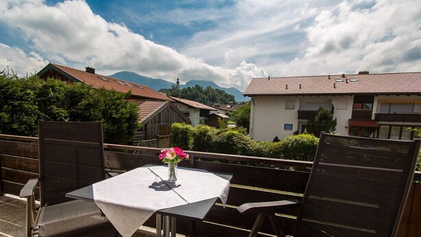 Un patio esterno con tavolo e sedie, un vaso con fiori e vista su case e montagne sullo sfondo.