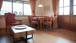 A dining area with a wooden table and chairs, a radiator, and a window with curtains. - Two-room apartment 5, approx. 40sqm with spacious balcony and mountain view (Reit im Winkl)