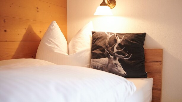 A bed with white bedding, a wooden headboard, and a wall-mounted lamp. - Two-room apartment 5, approx. 40sqm with spacious balcony and mountain view (Reit im Winkl)