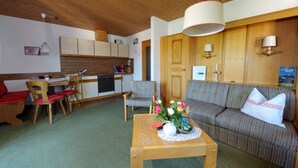 A cozy living area with a sofa, a dining table, and a kitchen in the background. - Ferienwohnung Nr. 3 Untersbergblick, 1 bis 2 Personen, 45 qm, 1 Schlafzimmer, Wohnraum mit Schlafcouch, Balkon (Schönau am Königssee)