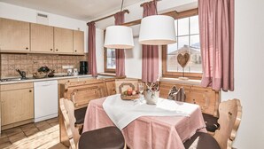 A kitchen with wooden cabinets, a dining table with a pink tablecloth, and a window with pink curtains. - (5) Zwei-Raum-Ferienwohnung 50qm, Dusche/WC, Extra-Schlafraum, Küche, Balkon (Reit im Winkl)