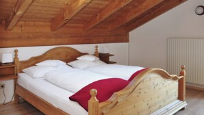 A wooden bed with white linens and a red blanket in a room with wooden beams on the ceiling. - Ferienwohnung Hochsalwand, 2 bis 4 Personen, 1 separates Schlafzimmer, 2. OG, Ostbalkon (Bad Feilnbach)