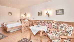 Una habitación con una cama, una mesa de madera con mantel blanco, un sofá floral e iluminación en la pared.