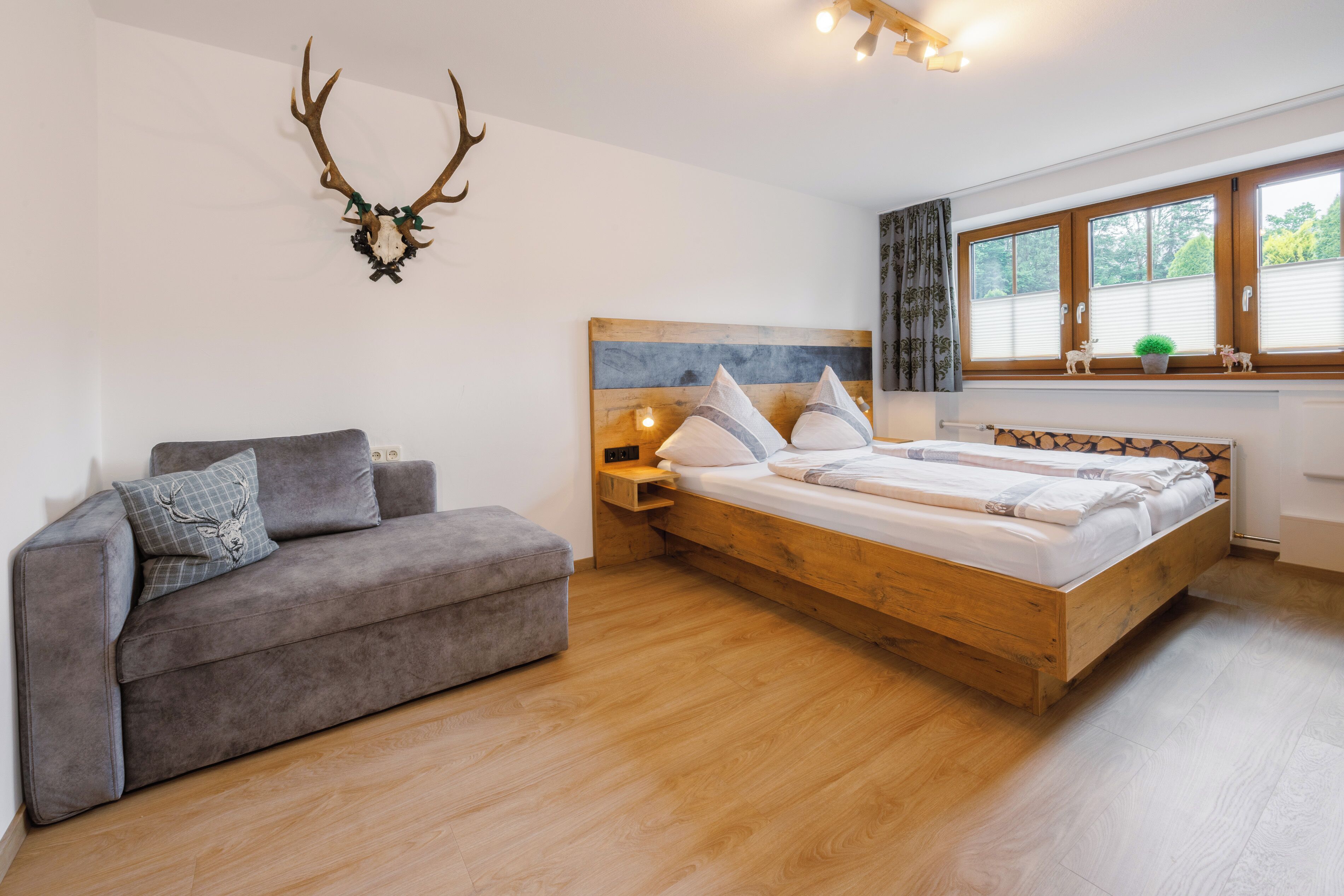 Ein Schlafzimmer mit einem hölzernen Bett, einem grauen Sofa und einer Dekoration aus Hirschgeweihen an der Wand.
