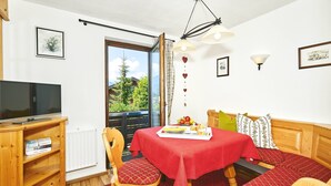Ein gemütlicher Essbereich mit einem Tisch für zwei Personen, einem Fernseher auf einem Holzständer und einem Fenster mit Blick auf Grünflächen.