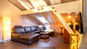 A cozy loft-style living room with a dark leather sofa, a small coffee table, and a TV mounted on the wall.