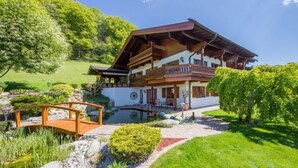 A two-story chalet with a wooden balcony, surrounded by a well-maintained garden and a small pond.