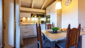 A modern kitchen with white cabinets, a wooden dining table, and a clock on the wall.