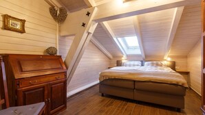 A cozy attic bedroom with a sloped ceiling, a wooden bed, a nightstand, a dresser, and a small chair.