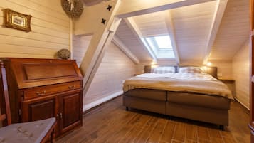 Ein gemütliches Schlafzimmer im Dachgeschoss mit schrägen Wänden, einem Holzbett, einem Nachttisch, einer Kommode und einem kleinen Stuhl.