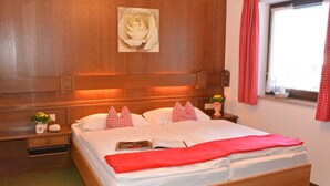 Una cama bien hecha con una colcha roja, un cabecero de madera y un cuadro de rosas colgado en la pared.