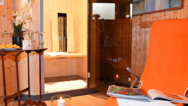 Un cuarto de spa con interior de madera, una camilla de masaje, una mesita con una vela y una revista.