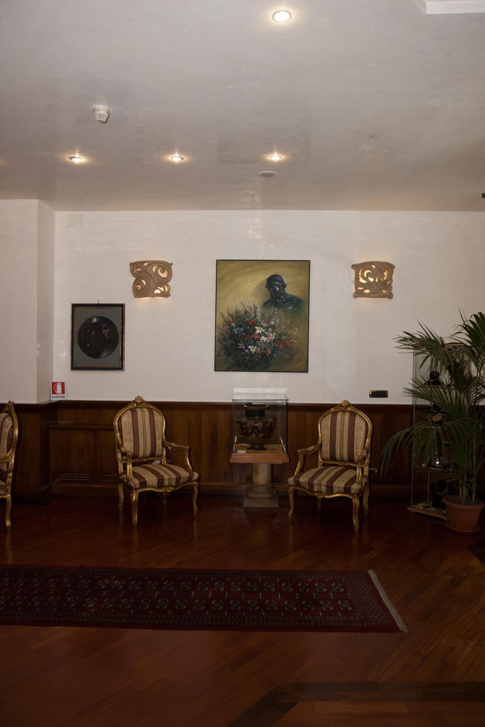 Um hall de entrada com duas poltronas estofadas, um balcão de recepção de madeira, um quadro emoldurado e um vaso de plantas.
