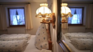 Hotellihuoneessa on kaksi sänkyä, joissa kummassakin on kukkakuviollinen tyyny ja valkoinen peitto. Yöpöydällä on avoin kirja. Huoneessa on seinään kiinnitetty lamppu ja peili, joka heijastaa huoneen sisustusta.