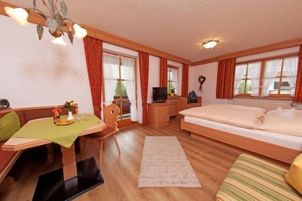 Een gezellige slaapkamer met een bed, een bureau met stoel, een tafel met een groene tafelkleed en een televisie op een houten kast.