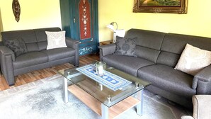 A living room with two grey sofas, a glass coffee table, a decorative cabinet, and a framed landscape painting on the wall.