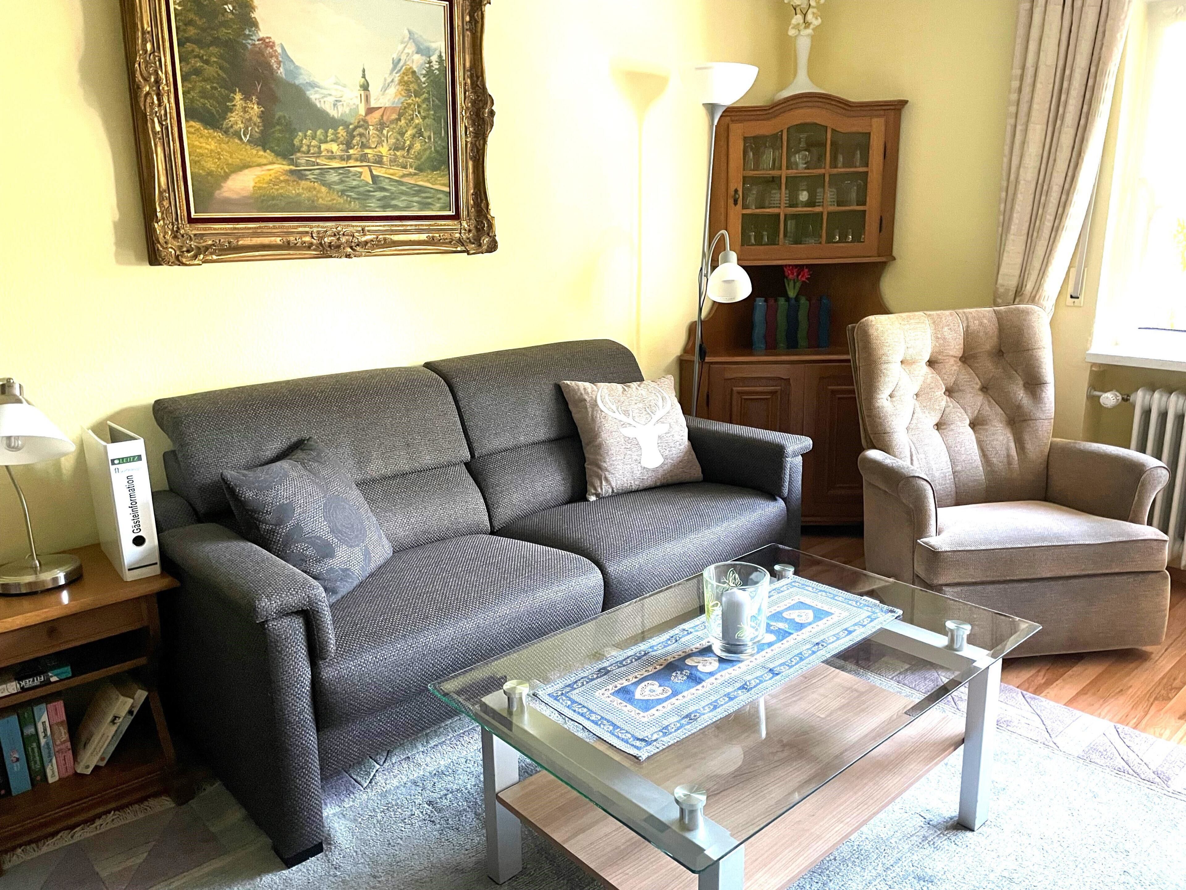A living room with a grey sofa, a glass coffee table, a wooden cabinet, and a framed painting on the wall.