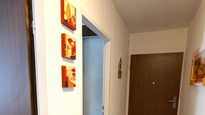 A hallway with a wooden door, a blue door, and a brown door. There are three framed pictures on the wall.