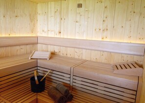 Una sauna con panche in legno e un catino nero.