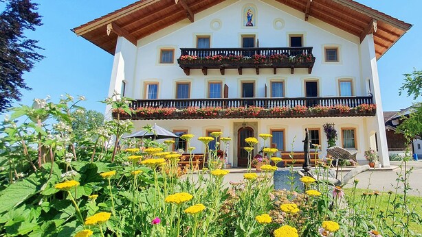 Un edificio di due piani con un balcone, circondato da un giardino pieno di fiori diversi.
