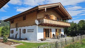 Una casa de madera de dos pisos con balcón, antena parabólica y mobiliario exterior.