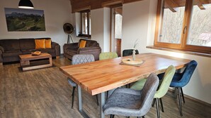 Una sala de estar acogedora con una mesa de comedor de madera, sillas con cojines y un sofá con almohadones anaranjados.