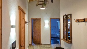 Un estrecho pasillo con pisos y paredes de madera, una puerta de madera, un banco y una lámpara colgante.
