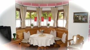 Una habitación acogedora con una zona de estar con banco de madera, una mesa redonda y un televisor sobre un mueble de madera.