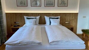 Een tweepersoonsbed met witte lakens, twee nachtkastjes met lampen, en drie ingelijste kunstwerken aan de muur.