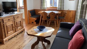Een gezellige woonkamer met een houten kast, een zwarte bank, een eettafel met stoelen en een televisie.