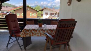An outdoor patio with a table and chairs, a potted plant, and a view of houses and mountains in the background. - (2) Zwei-Raum-Ferienwohnung 40qm, 1-4 Personen, Extra-Schalfzimmer, Wohnküche, große Balkonterrasse (Reit im Winkl)